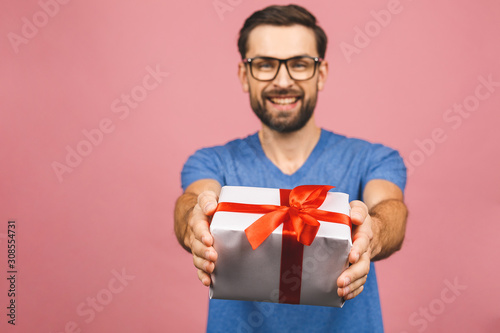 Wonderful gift! Adorable photo of attractive man with beautiful smile holding his birthday present box isolated over pink background. © denis_vermenko
