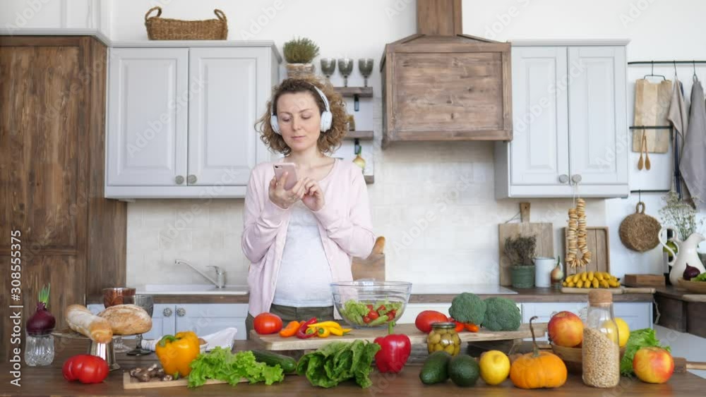 Pregnant Woman Cooking Healthy Food On Kitchen And Using Smartphone. Pregnant Woman Cooking Healthy Food On Kitchen And Using Smartphone.