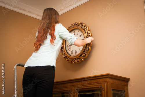 Young woman hanging a clock on the wall