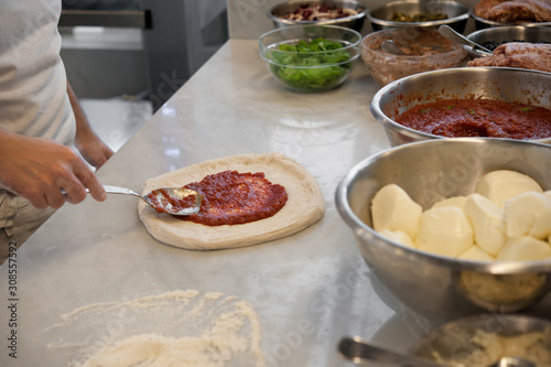 Preparing Pizza Margherita on a marble top. Pizzaiolo puts tomato sauce over a raw pizza dough. Selective focus. 