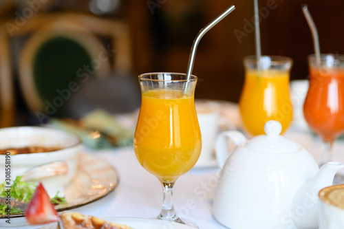 morning Breakfast or brunch in the restaurant. table with drinks and food. a glass of fresh orange juice and a metal drinking straw. selective focus
