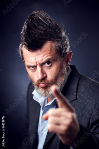 A portrait of bearded man with iroquois wearing suit showing finger at camera. People and emotions concept
