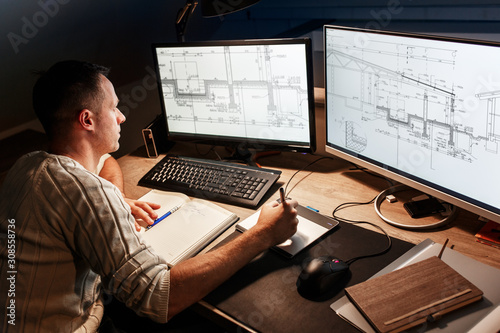 Engineer working at home. He's using a digital pen and examining the blueprint on screen. photo