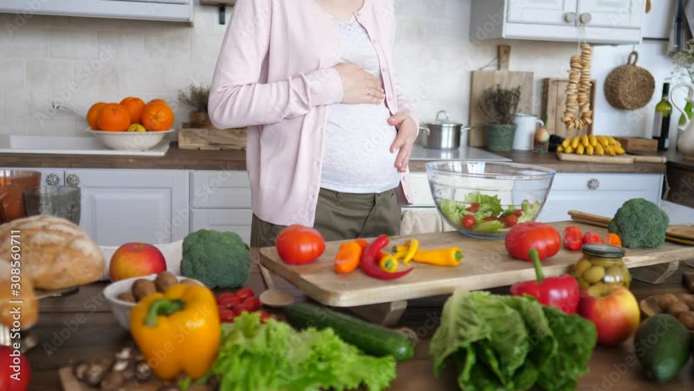 Pregnant Woman Touching Her Belly While Cooking Healthy Salad On Kitchen. Pregnant Woman Touching Her Belly While Cooking Healthy Salad On Kitchen.