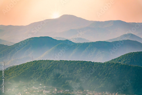 Layers of mountains in the haze during sunset. Beautiful sunset in the mountains. Beautiful sunset in a hilly valley with villages and fog in the lowlands. © Dmitrii Potashkin