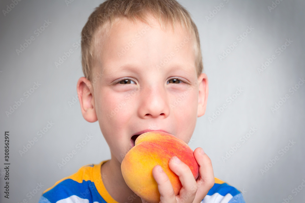 Happy child eating fresh bio sweet peach. Little boy bites ripe natural fruit and smiles. Concept of caring for healthy children?s food. Vitamins for babies. Portrait of vegetarian toddler indoors Happy child eating fresh bio sweet peach. Little boy bites ripe natural fruit and smiles. Concept of caring for healthy children?s food. Vitamins for babies. Portrait of vegetarian toddler indoors