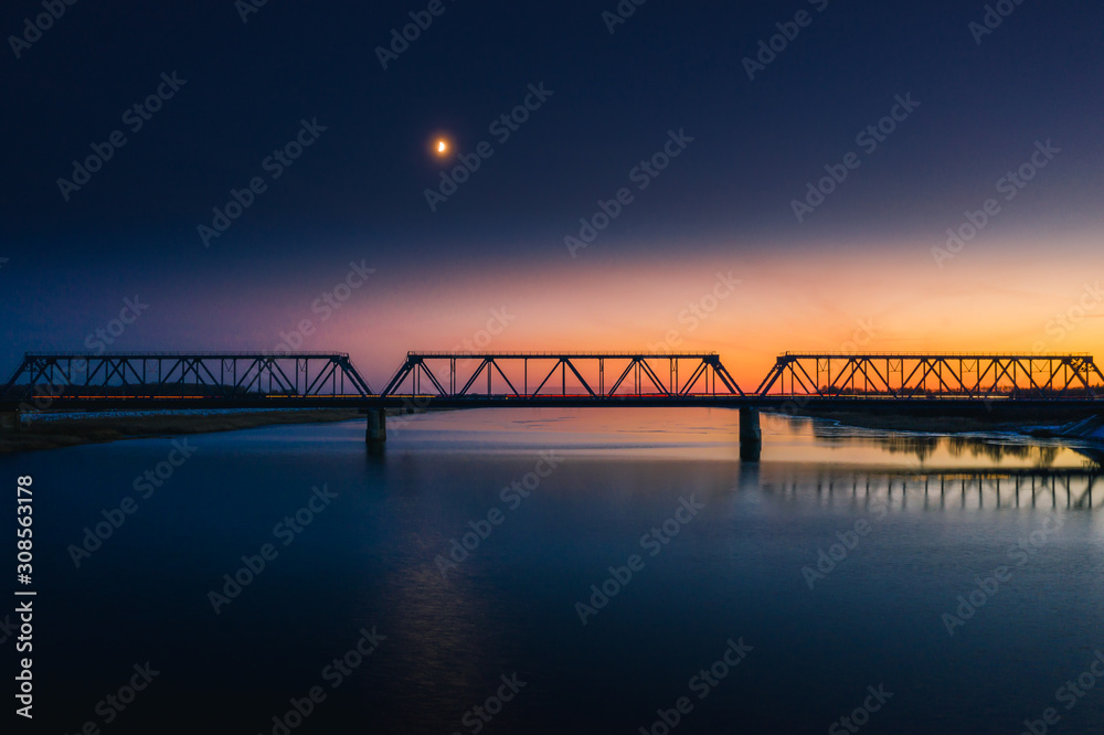 Aerial view on railroad bridge at sunset with moving cars. Steel construction silhouette on a colorful sky background. 