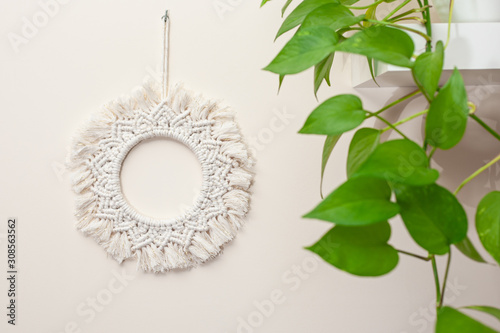 Handmade cotton macrame mandala wall decoration hanging on a wall with green leaves