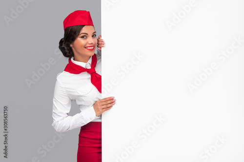Cuadro en lienzo Cheerful air hostess peeking out from behind blank banner