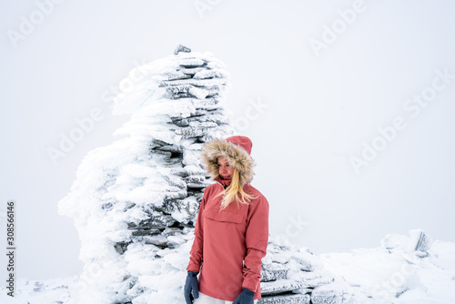 Portrait of blonde hiker girl with fur hooded jacket and backpack outdoors in the mountains with snow. Wilderness, winter time, explorer and travel concept.