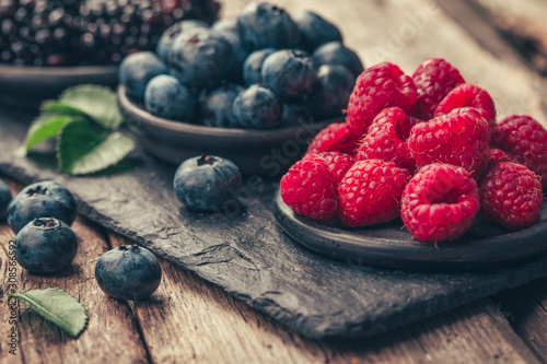 Fresh berries with raspberries, blueberries, blackberries in bowl on a stone stand on wood background. photo