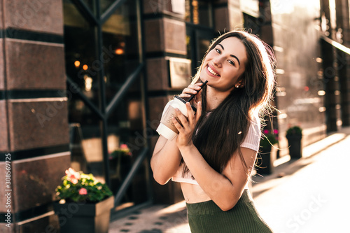 Beautiful smiling woman drink coffee walking on the city in summer day.