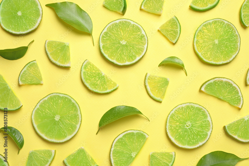 Juicy fresh lime slices and green leaves on yellow background, flat lay