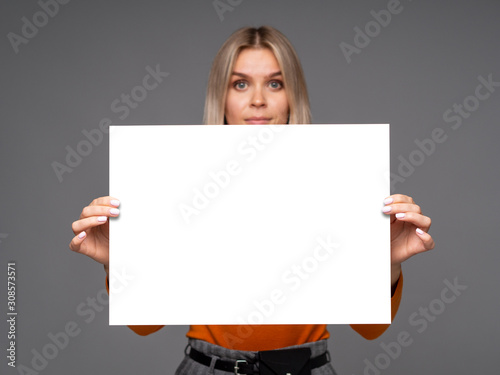 Gorgeous young woman holding a mockup vertical A1 white paper sheet with copy space for text