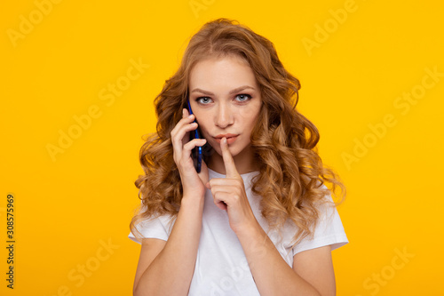 Blond curly hair woman posing with silence getsure holding phone photo