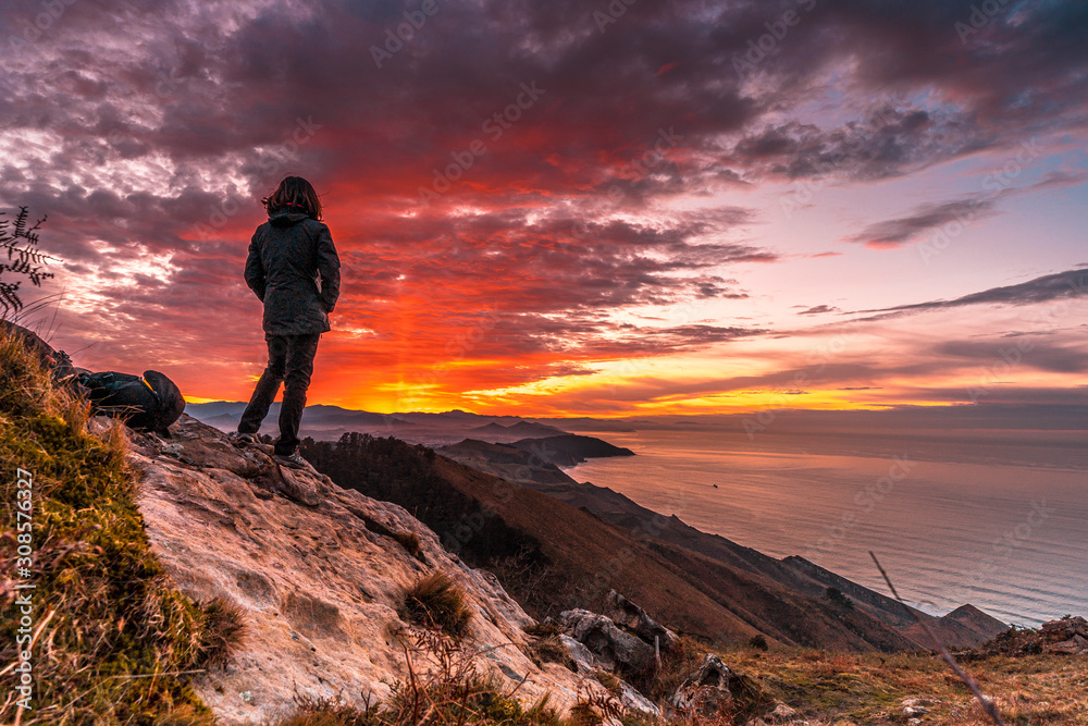 A young woman in the incredible orange sunset on the winged Mount Jaizkibel of San Sebastian. Basque Country