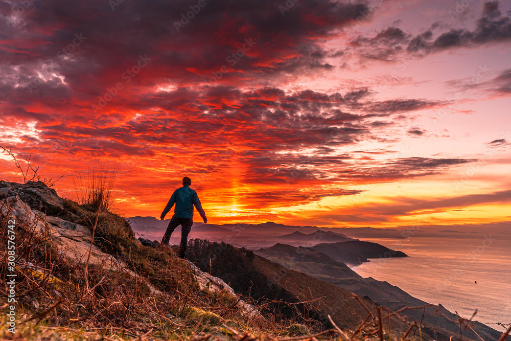 Obraz premium A young man in the incredible orange sunset on the winged Mount Jaizkibel of San Sebastian. Basque Country