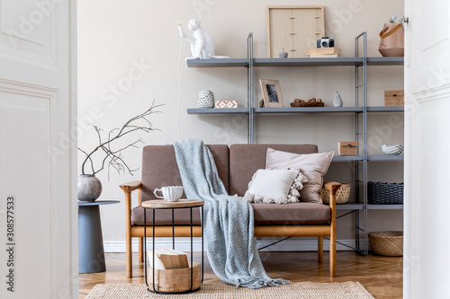 Interior design of living room with brown wooden sofa, gray bookstand, coffee table, plaid, pillows, decoration and elegant accessories. Beige and japandi concept. Stylish home staging. Template. 