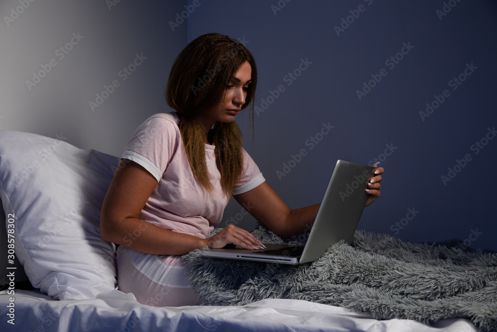Depressed serious woman sitting in he bed and working on the laptop Depressed serious woman sitting in he bed and working on the laptop
