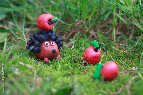 Wallpaper Mural Plasticine world - small homemade hedgehog with apple on his back on a green meadow surrounded plasticine red apples, selective focus on the hedgehog Torontodigital.ca