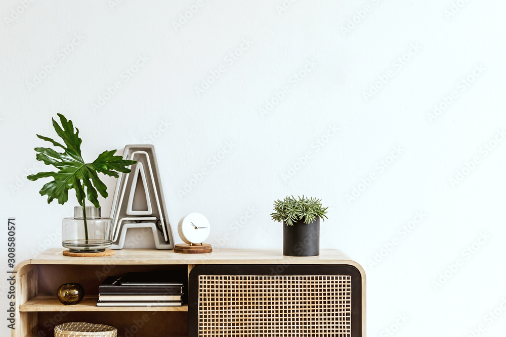 Obraz Interior design of living room at scandinavian apartment with stylish commode, plant, tropical leaf, books, big letter, white clock and elegant accessories. Modern home decor. Template. Copy space.