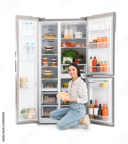 Young woman with corn near open refrigerator on white background