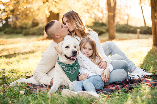 Happy beautiful family with dog labrador is having fun are sitting on green grass in park.