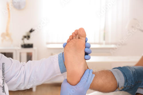 Male orthopedist checking patient's foot in clinic, closeup photo
