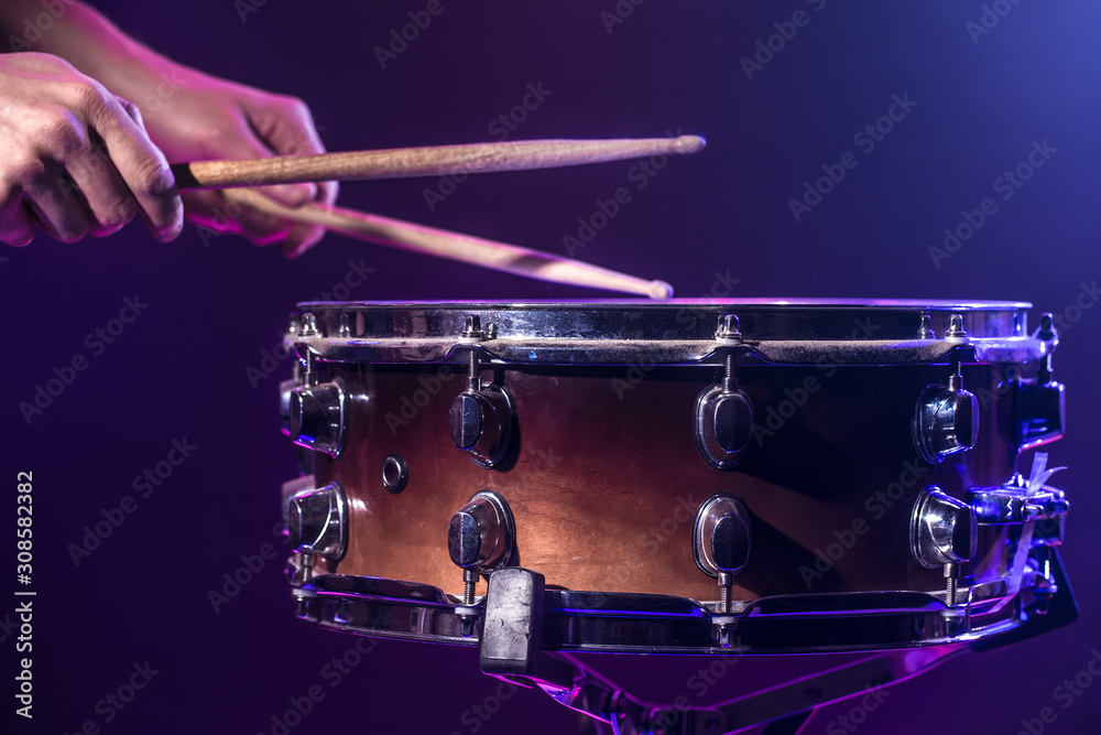 Obraz premium The drummer plays the drums. Beautiful blue and red background, with rays of light. Beautiful special effects smoke and lighting. Process of playing a musical instrument. Close-up photo.