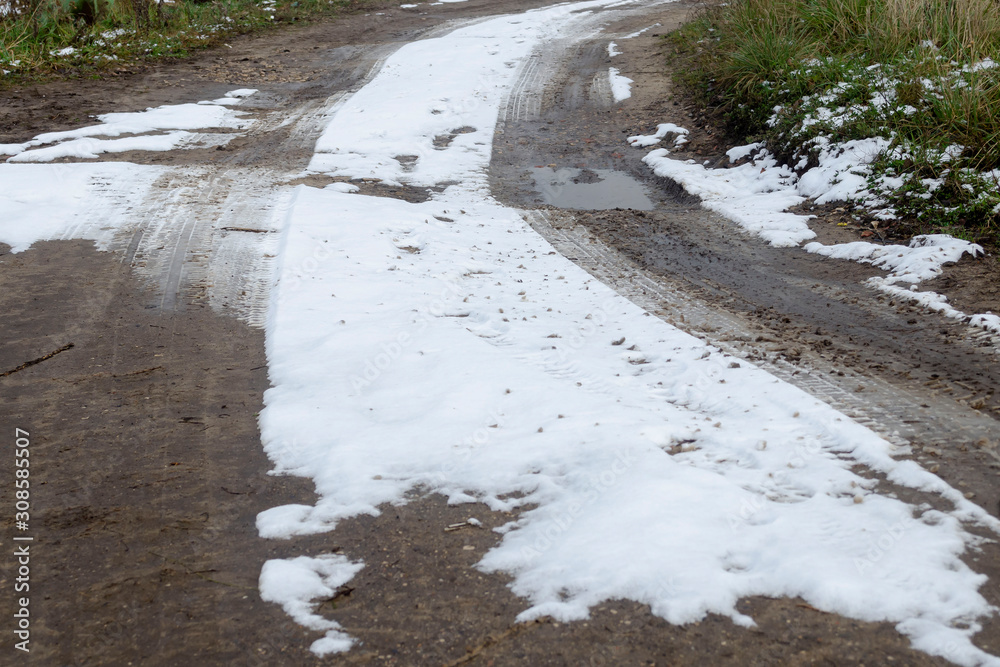 Fototapeta premium Muddy road, snow covered street in the countryside after snowfall. Winter landscape with rural road,