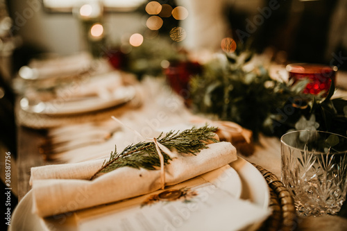Christmas table setting for traditional lunch or dinner on a rustic table with seasonal greeting cards, tableclothes, tableware and festive decorations. Concept of family traditions and celebrations