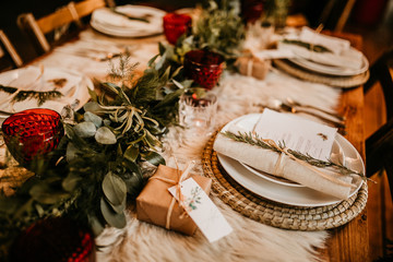Christmas table setting for traditional lunch or dinner on a rustic table with seasonal greeting cards, tableclothes, tableware and festive decorations. Concept of family traditions and celebrations