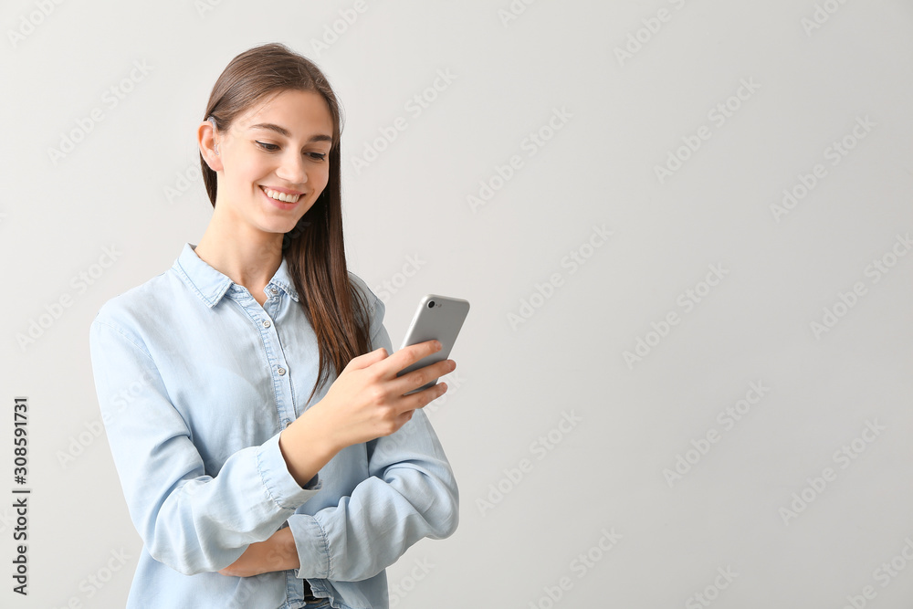 Young woman with hearing aid and mobile phone on light background Young woman with hearing aid and mobile phone on light background