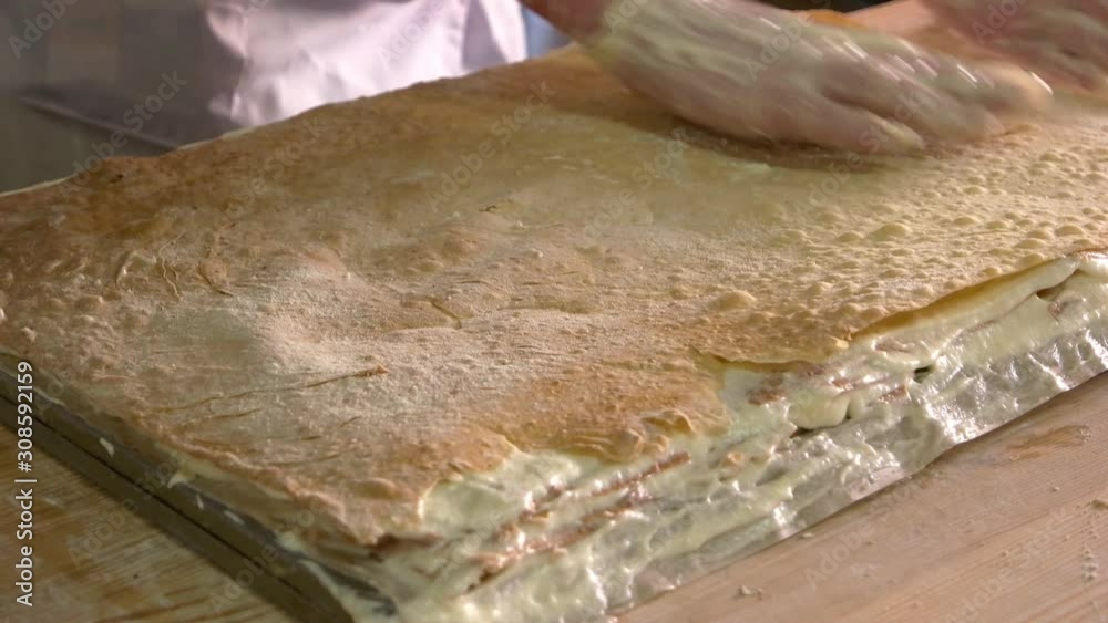 Confectioner making napoleon cake. Hands of the pastry chef in the cooking process. Layered dessert with crispy dough and buttercream. Confectioner making napoleon cake. Hands of the pastry chef in the cooking process. Layered dessert with crispy dough and buttercream.