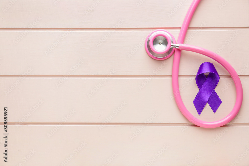 Purple ribbon as symbol of World Cancer Day and stethoscope on wooden background
