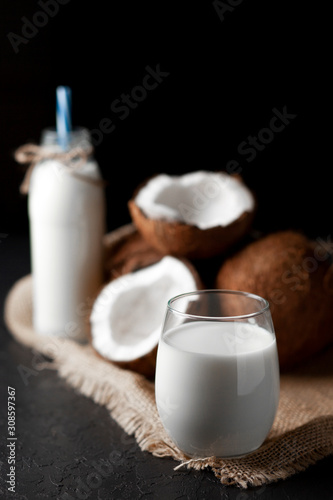 fresh coconut milk in a glass against a dark background, cosmetic cream from coconut on a cloth