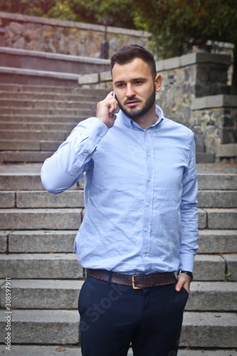 Portrait of a bearded man near the big steps of an old European castle. Businessman talking on the phone. Fashionable guy with stylish clothes.