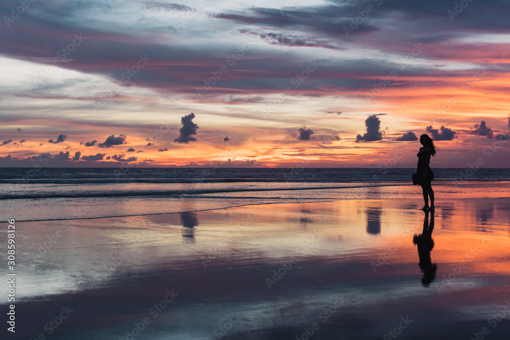 BALI, Indonésia: por do sol na praia de Seminyak e silhueta de mulher. Céu colorido..