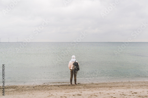 One caucasian man young caucasian woman tourist with a black backpack on a sandy beach near the Baltic sea in winter. Theme trip alone. Thoughts and dreams overlooking the horizon