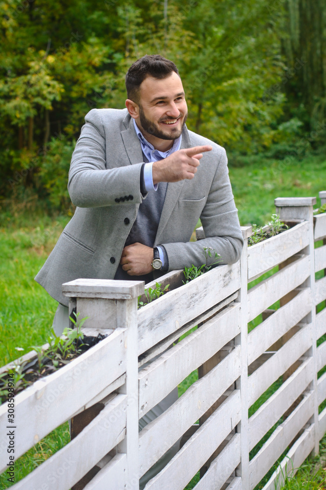 Portrait of a sexy man dressed in a suit. Fashionable guy in the autumn nature near a white wooden fence. Businessman relaxes. Skok photo for design Portrait of a sexy man dressed in a suit. Fashionable guy in the autumn nature near a white wooden fence. Businessman relaxes. Skok photo for design