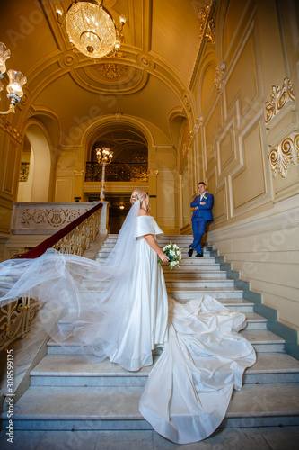 Beautiful wedding couple walking a gorgeous stairs holding hands and looks to each other. In opera