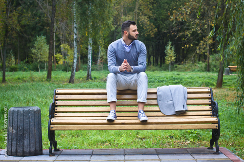 Young sexy guy sitting on a bench in an autumnal, summer park. A man contemplating new ideas while walking. European countryside. Stock Photo