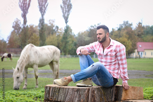 Young handsome guy Cowboy. farmer is sitting on a large stump on his ranch. Rural landscapes, countryside. Trees, field, farm. Stock photos for design. photo