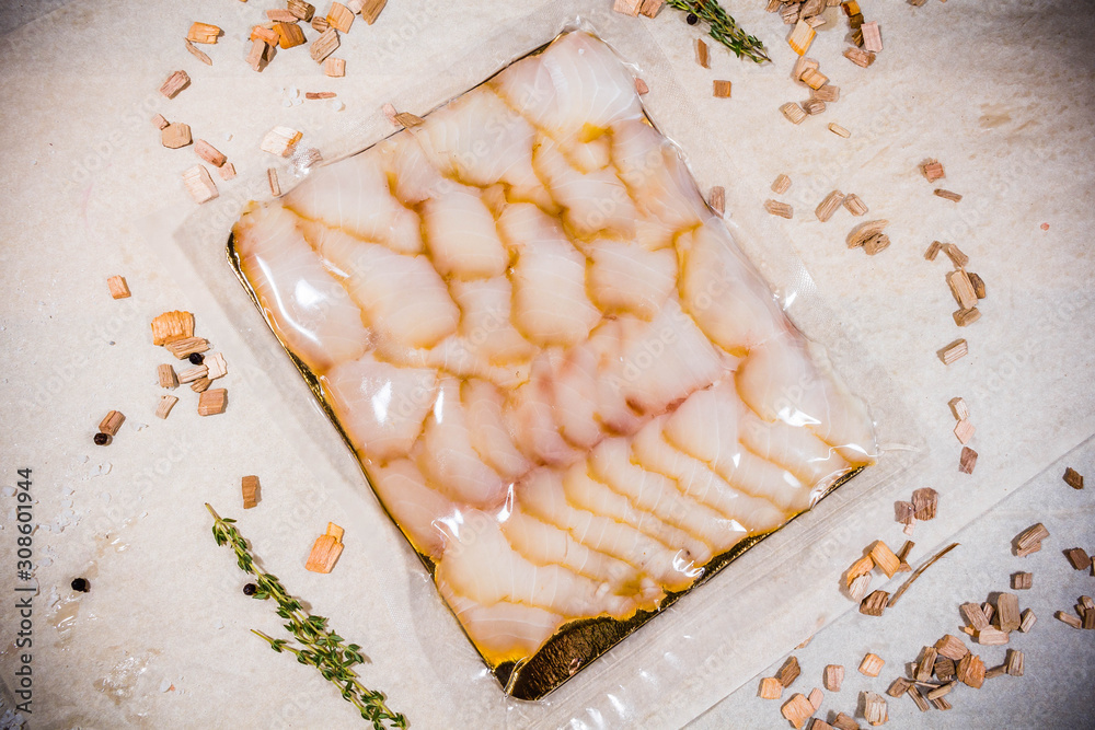 White smoked fish in a sealed vacuum package on the background of chips for smoking White smoked fish in a sealed vacuum package on the background of chips for smoking