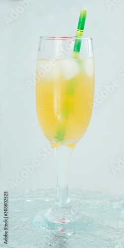 champagne glass with cocktail, juice with ice green straw on water light background