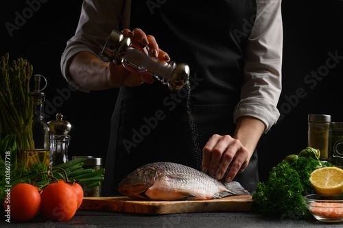Canvas Print Chef cooks fresh fish on the background with ingredients, salts it before cookin