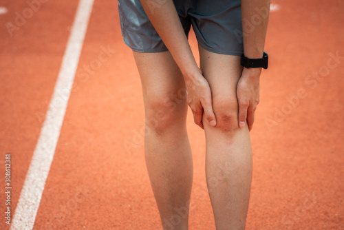 Close-up of sport woman holding her knee, suffering from injury, she had bruise on her knee. Injured after runner falling or impact running track floor.