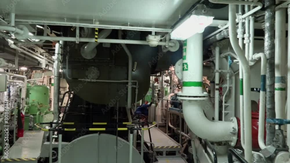 tanker crew in blue protection uniform works in machinery room with multiple closed conduits and pumps distant shot tanker crew in blue protection uniform works in machinery room with multiple closed conduits and pumps distant shot