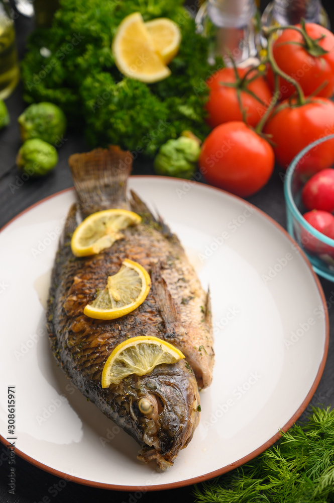 Tasty fish cooked with lemons on a background of fresh vegetables.Vertical frame Tasty fish cooked with lemons on a background of fresh vegetables.Vertical frame