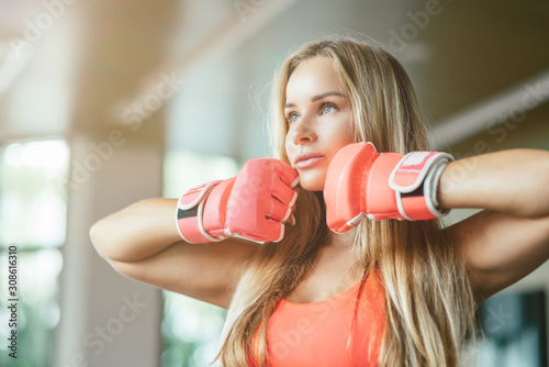 Close up portrait of sexy fit blonde in stylish sportswear and kickboxing gloves keeping hands near her face and looking aside. Sporty girl, Thai boxing, mma concept. Horizontal shot